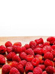 Pile of fresh raspberry on a wooden board, white background. Vertical image. Top quality fruit.