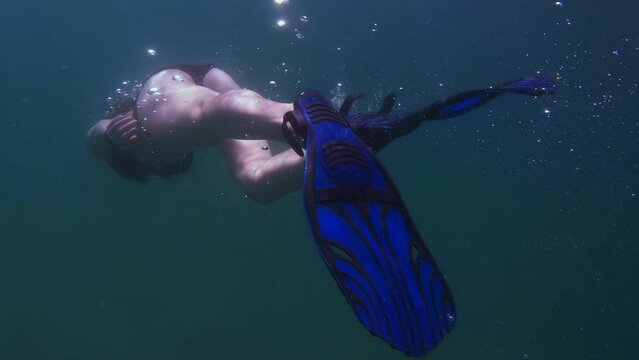a girl is engaged in freediving, a woman is swimming underwater in the open ocean, slow motion
