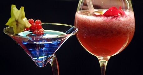 Blue cocktail and red non-alcoholic cocktails with fruit toppings isolated on black background