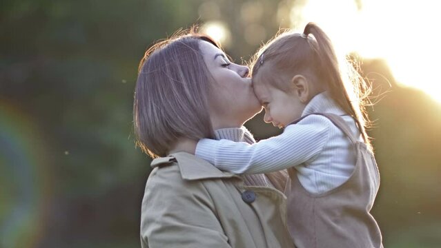 An adorable, sweet little girl hugs her young mother during a walk in a spring park.