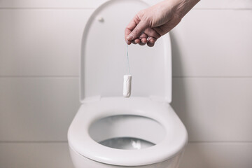 Woman's hand with a menstrual tampon over the WC
