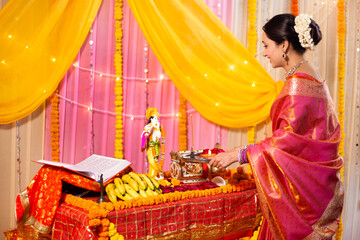 Ethnic Indian woman praying Lord Krishna -  Spiritual concept. A lady wearing red saree is holding a pooja/puja thali and doing aarti of Ganesh idol on Ganesh festival - Hindu culture religion