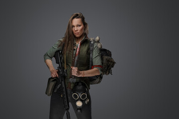 Portrait of female killer with gun and knife carrying backpack against grey background.