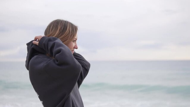 A female tourist puts the hood of a sweatshirt over her head and looks at the ocean