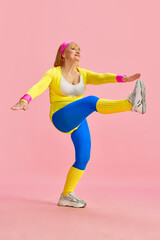 Sportive middle-aged, mature woman in colorful sportswear training, rising legs to hands, posing against pink studio background. Concept of sportive lifestyle, retirement, health care, wellness. Ad