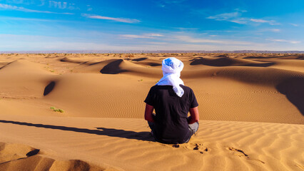 Rear view of man with white turban looking at panoramic view of desert - obrazy, fototapety, plakaty