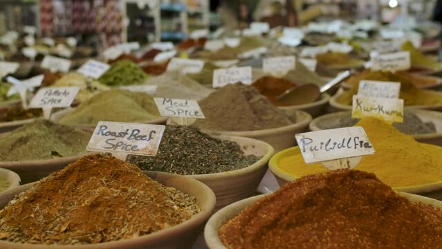 Many different spices for sale inside bowls at a local shop, each for a specific dish (roast beef, curcuma, cinnamon, ginger). Slow motion panning shot.