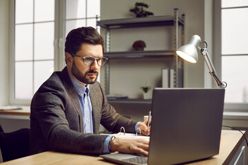 Serious businessman working on laptop in modern office. Focused confident middle-aged man in formal...