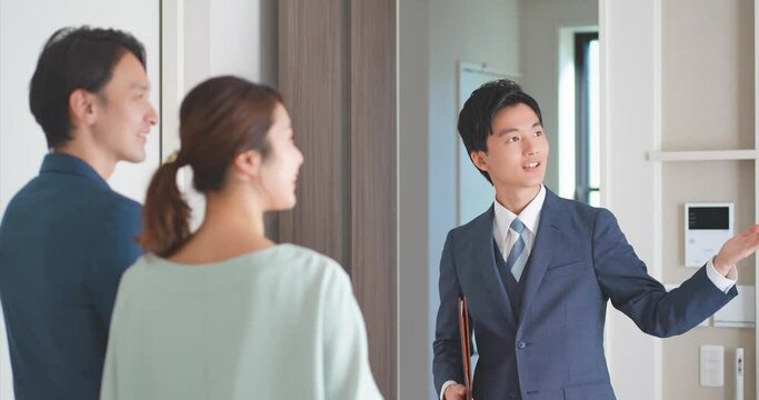 30代夫婦にモデルハウスを案内する不動産営業マンの若い男性