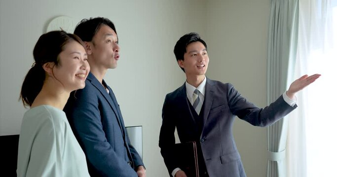 30代夫婦にモデルハウスを案内する不動産営業マンの若い男性
