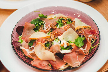 Salad with herbs, arugula, prosciutto, cheese, green olives and nuts.