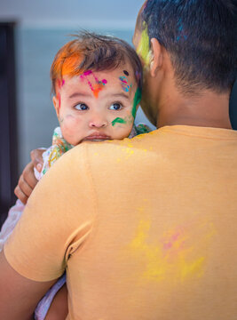 cute infant resting head at father shoulder at holi celebration from flat angle