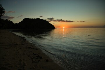 Fototapeta premium Picturesque golden yellow orange sunset on Coron beach in the Philippines, hills in the background.