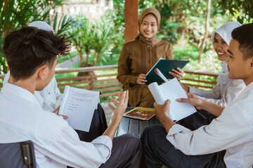 A student reads his assignment and the others listen during outdoor class in the gazebo