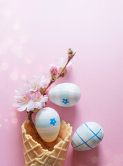 Easter eggs, cherry blossom flowers, waffle cone on a pink background with bokeh and copy space. Vertical photo