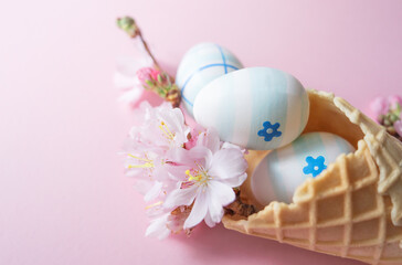 Close up of easter eggs, cherry blossom flowers, waffle cone on pink background with copy space