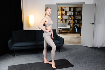 A cute slender girl is preparing for yoga training. Girl standing on yoga mat at home in living room