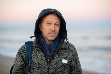 Handsome mature man at the beach, outdoor portrait. Attractive happy smiling adult male model posing at seaside, sunset or sunrise time