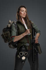 Fototapeta na wymiar Portrait of female killer with gun and knife carrying backpack against grey background.