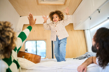 young interracial family spending quality time together with their daughter, who has a lot of fun in a bright camper van