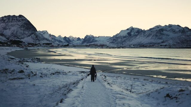 A person handling a tripod is going on the beach in lofoten islands in winter