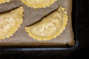 Cooking meat turnovers or pies, or empanadas, or cornish pasty. Unbaked shortcrust pastry,  egg washed, on a baking tray.