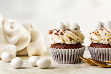 Easter chocolate cupcakes with cream cheese, sweet candy eggs and nest. Holiday homemade dessert. Light background.