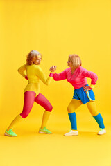 Fototapeta na wymiar Arm wrestling. Two elderly sportive women in colorful uniform training, posing against yellow studio background. Concept of sportive lifestyle, retirement, health care, wellness. Ad