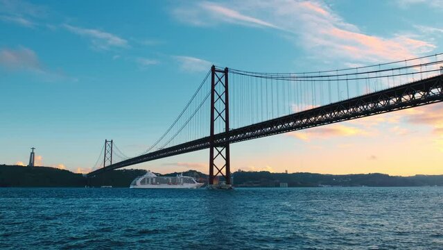 View of 25 de Abril Bridge famous tourist landmark of Lisbon connecting Lisboa to Almada on Setubal Peninsula over Tagus river with cruise liner passing under. Lisbon, Portugal