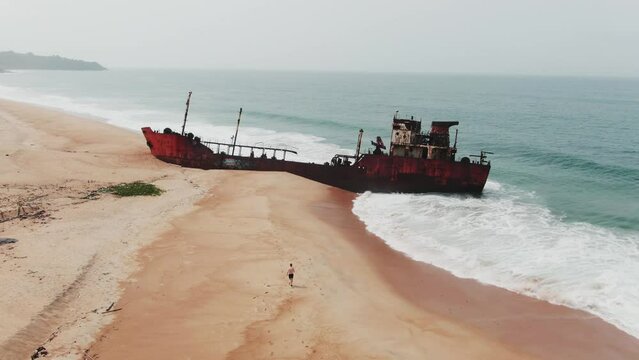 a tourist walking towards a shipwreck on the west african coast in Robertsport, Liberia