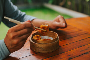 Men's hands hold the roasted shrimp in dim sum with sticks. A man eats delicious Asian food