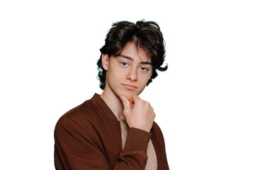 Thoughtful handsome teenager in brown jacket touching chin makes choice looks at camera stands against transparent background. Confident Italian boy posing at studio. Male model.