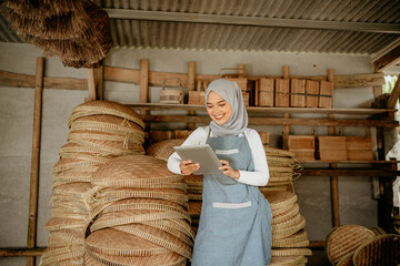 attractive muslim woman using tablet to check her traditional bamboo products stock at online shop