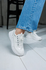Female legs in white stylish sneakers. Casual women's fashion. Comfortable shoes for women. Women's comfortable summer shoes.