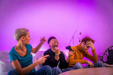 Group of young friends playing video games together on the sofa at home, purple led, man wins