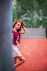 Beautiful girl with long red hair. Girl on vacation. The girl goes in for sports. On a Sportsground. Girl and palm trees. Girl in a short skirt