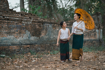 Mother and daughter dressed in traditional costumes with an umbrella walking at Wat Mon Jam Sil...
