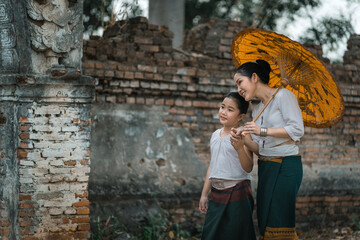 Mother and daughter dressed in traditional costumes with an umbrella walking at Wat Mon Jam Sil Temple of ancient Burma according to Thai culture in Lampang Northern Thailand.
