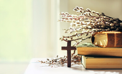 Fototapeta na wymiar wooden cross, old biblical books and willow twigs close up on table, abstract light background. Orthodox palm Sunday, Easter holiday. Symbol of Christianity, Lent, Faith in God, Church. copy space
