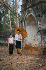 Fototapeta premium Mother and daughter dressed in traditional costumes with an umbrella walking at Wat Mon Jam Sil Temple of ancient Burma according to Thai culture in Lampang Northern Thailand.