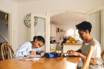 Daughter doing homework, mother working on laptop