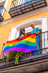 Lesbian girl couples with lgbt flag on balcony at home party, waving, LGBT pride