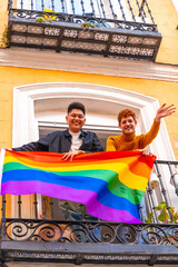 Obraz na płótnie Canvas Gay boy couples with lgbt flag on balcony at home party, waving smiling, LGBT pride