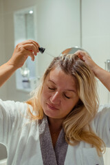  Woman applies oil to her hair with pipette. Beauty caring for scalp and hair. 