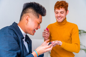 Beautiful gay couple doing makeup, painting their nails and having fun indoors at home, lgbt concept