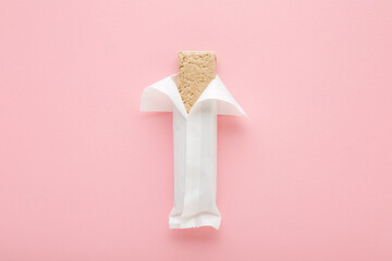 Halva bar on light pink table background. Pastel color. Opened white pack. Closeup. Sweet healthy...