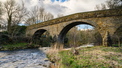 Fototapeta na wymiar River Derwent flows under Ebchester Old Bridge, formed by the meeting of two burns in the North Pennines and flows between the boundaries of Durham and Northumberland as a tributary of the River Tyne
