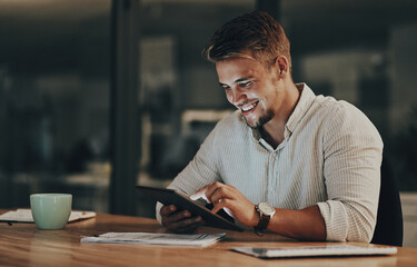 Rounding off another deadline. a young businessman using a digital tablet in an office at night.