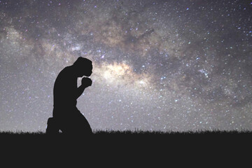 Man silhouette kneeling praying to god hopefully with the beautiful Milky Way - obrazy, fototapety, plakaty