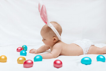A newborn baby with bunny ears and colorful Easter eggs on a white background. Newborn baby Easter bunny. Easter egg hunt. 